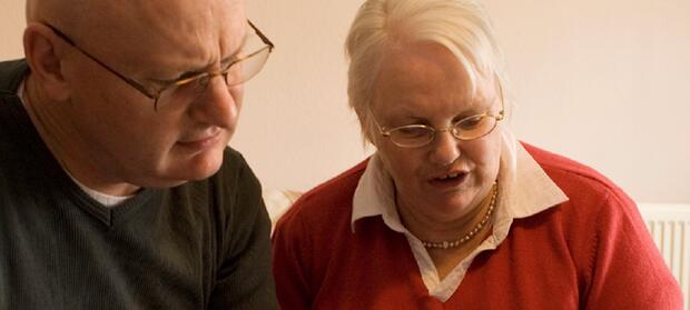 Man wearing glasses and green jumper stood next to woman wearing red jumper and glasses.
