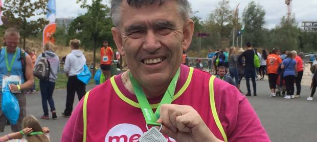 Man in Mencap running vest smiling holding a medal.
