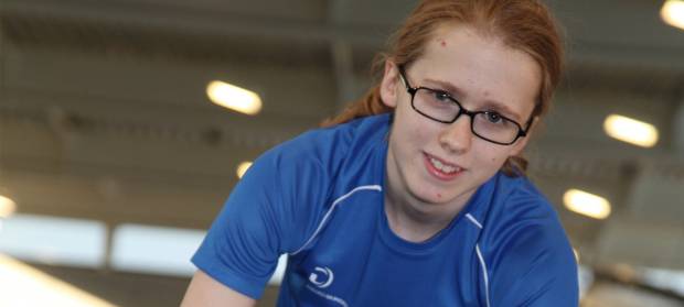 Young woman in gym wearing  a blue t-shirt and glasses.