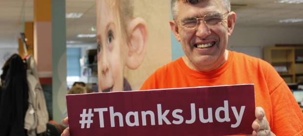 Man smiling at camera holding a sign that reads "#ThanksJudy"