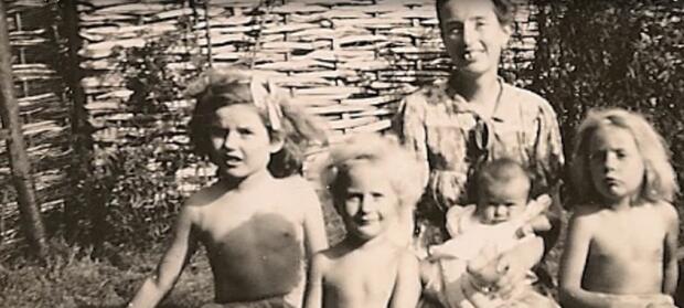 Black and white photo of mother sat outside with three children around her and baby on her knee