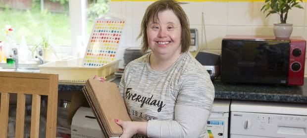 Smiling woman in kitchen holding placemats.