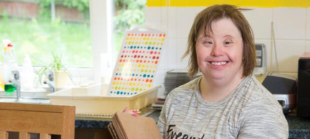 Smiling woman stood in kitchen holding placemats
