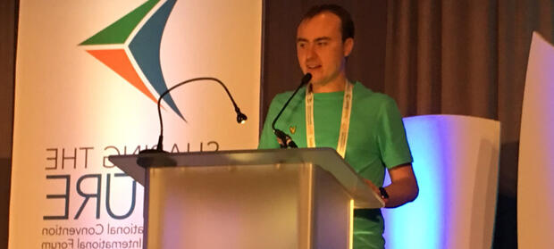 Young man stood at podium, speaking in to a microphone