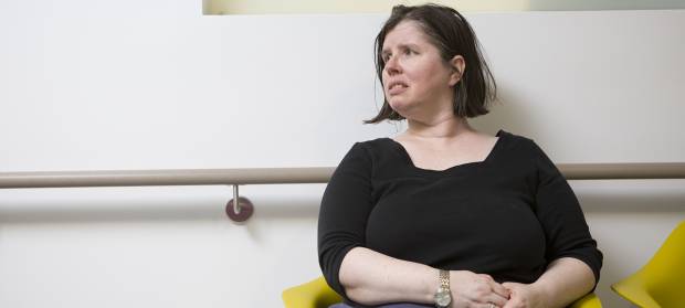 Woman with dark hair wearing a black top, sat in hospital waiting room.