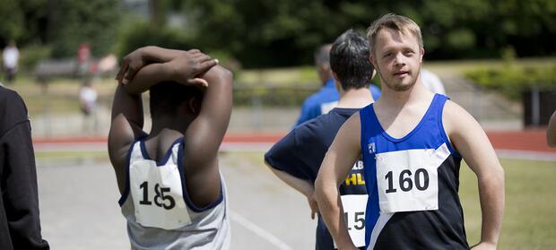Young man wearing running vest and number stood on running track.