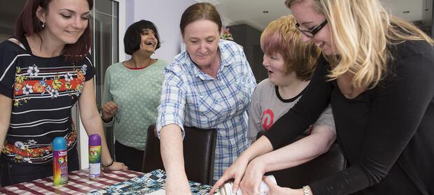 Group of five people stood around kitchen table.