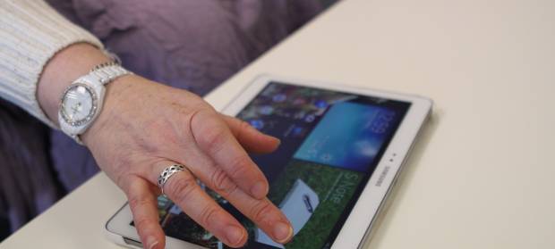 Person's hand using an iPad resting on a table.