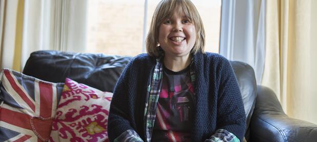 Woman with light hair sat on sofa smiling.