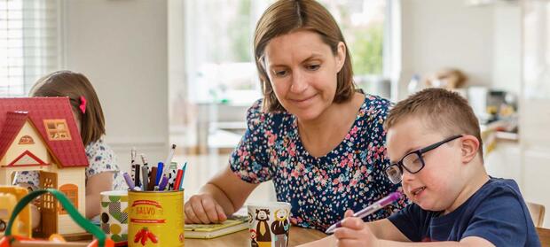 Mother sat at table with her song who is drawing.