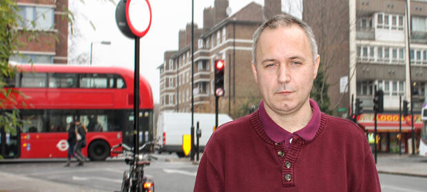Man stood on high street looking into camera, London bus moving in the background