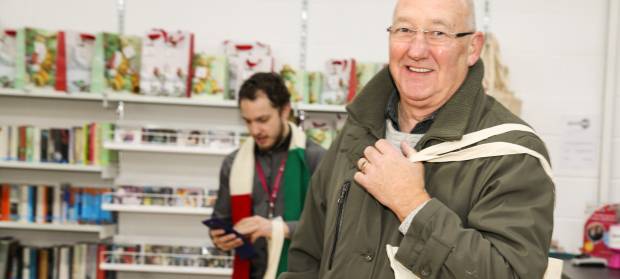 Man looking into camera whilst stood in Mencap charity shop and holding bag on his shoulder.