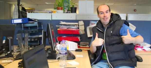 Man giving thumbs up sign sat at desk in an office.