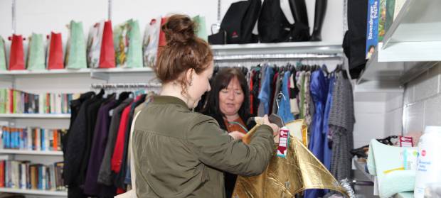 Two women in charity shop looking at items of clothing.