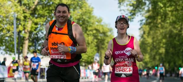 Woman wearing Mencap vest runs outside with male guide runner next to her