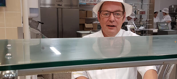 Person wearing white hat and uniform stood behind food preparation counter