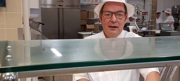 Person wearing white hat and uniform stood behind food preparation counter