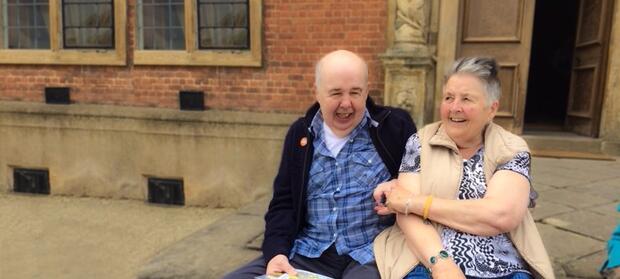 Older man and woman sat laughing together outside in front of old building