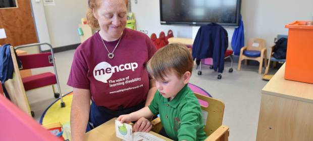 Woman wearing Mencap t-shirt sat next to young boy playing with picture cards.