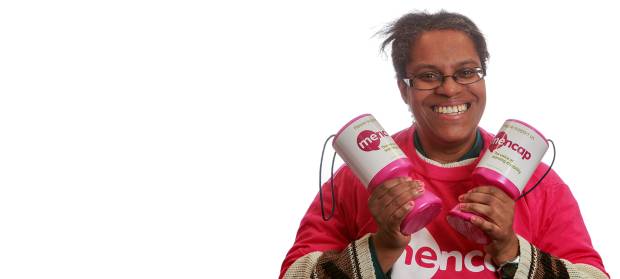 Woman smiling looking into camera. She is wearing a pink Mencap t-shirt and holding Mencap collection pots in her hands.