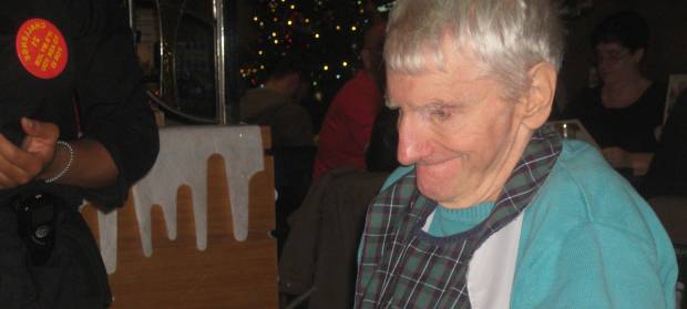 Old man with white hair smiling sat in restaurant