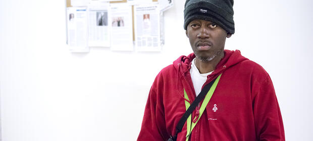 Man wearing black beanie hat and red jumper stood against white wall