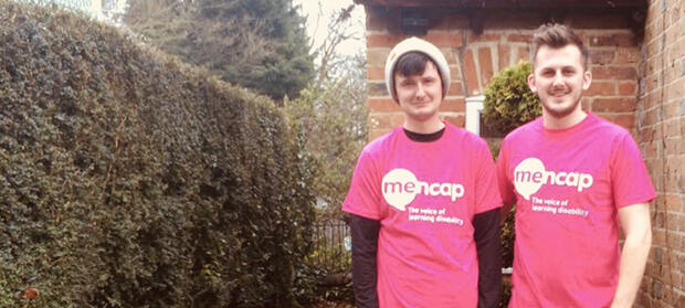 Two young men wearing Mencap t-shirts stood together in front of their house