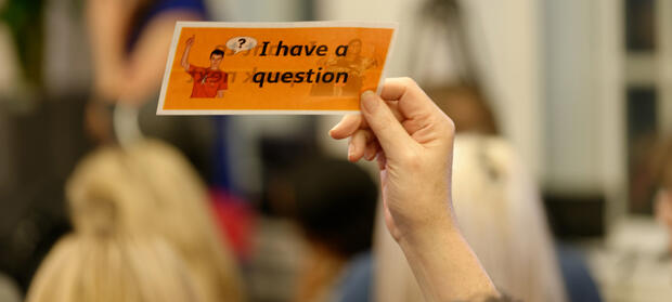 Hand holding up a sign which reads "I have a question".