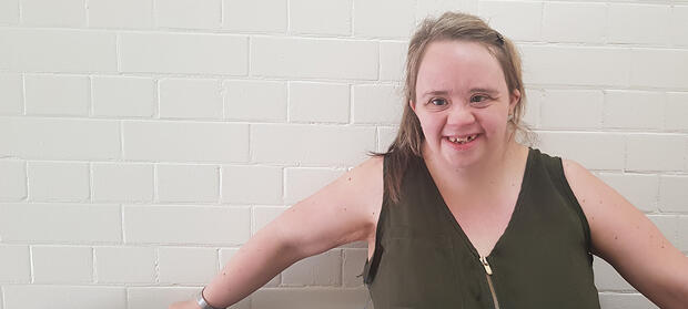 Woman with blonde hair wearing a green top stood smiling in front of a white brick wall