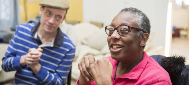 A man and woman sat next to each other in a Mencap service, playing with their hands.