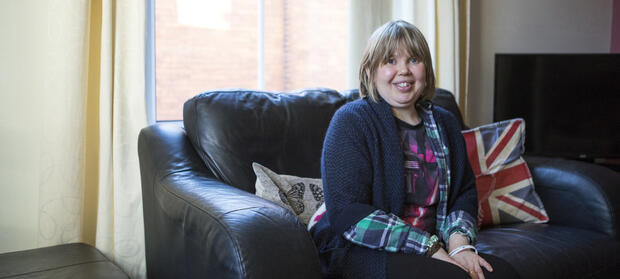 Woman with light hair sat on sofa smiling.