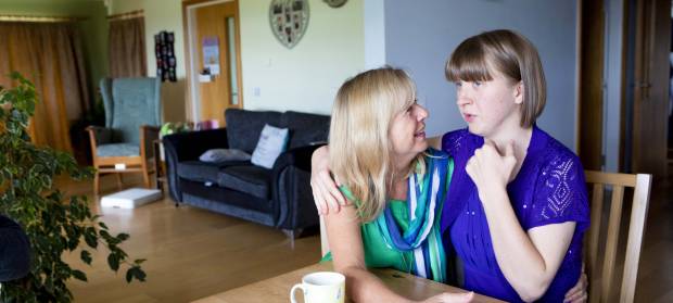 Mother and daughter with arms around each other, sat talking together at dining room table