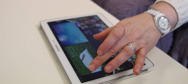 Hand with rings on hovering over iPad which is on a table.