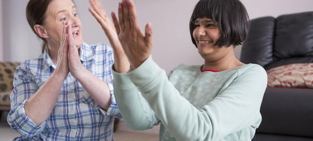 Two woman sat on floor in living room clapping their hands together.