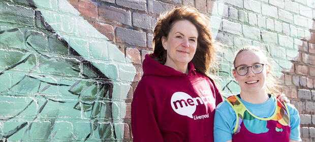 Two women stood together smiling in front of painted wall.