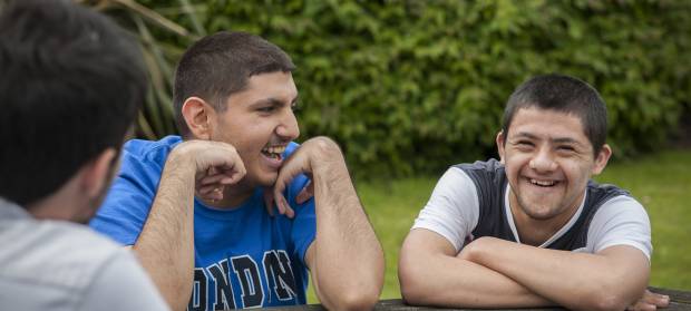 Two young men sat at picnic table outside laughing
