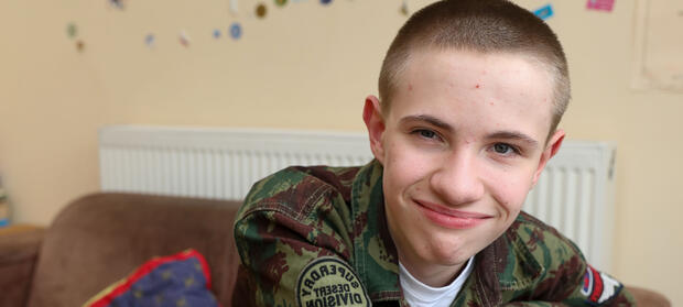 Young man, Alex, with short dark hair, wearing green jacket, smiling into camera.