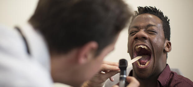 Man with his mouth wide open with a doctor looking into his throat.