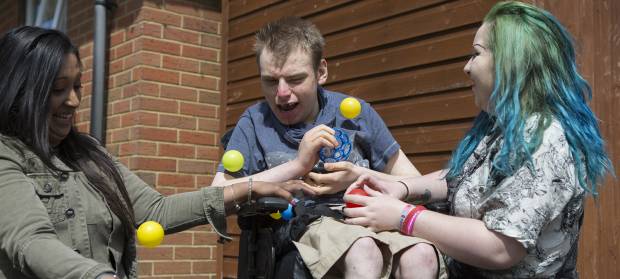 Three people sat outside in garden playing with yellow plastic balls.