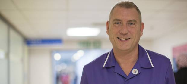 Male nurse stood smiling in hospital corridor