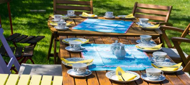 Photograph of a table in a garden set up for lunch with plates, tea cups and cutlery.