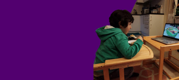 A young boy looks at a laptop while he eats