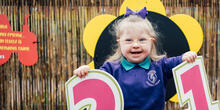 Young girl stood in play area smiling and holding up "2" and "1" number signs.