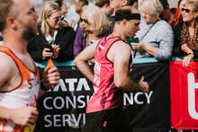 A man running in a Mencap running vest in front of cheering crowds who are lining the street on part of the course