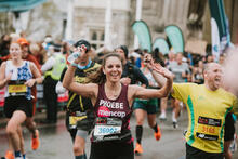 A female runner with Mencap running vest cheering with the crowds