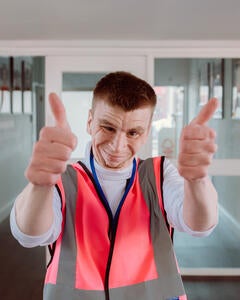 A man standing in a corridor with his thumbs up to the camera wearing a high visibility verst