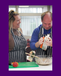 A woman showing a man with learning disabilities how to cook