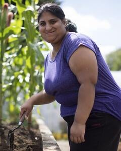 A woman standing in a garden smiling and holding a trowel. 