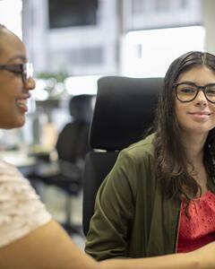 Two women working on a computer at a desk. 