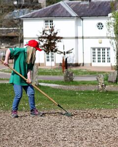 A girl in a red cap is raking gravel in someone's driveway